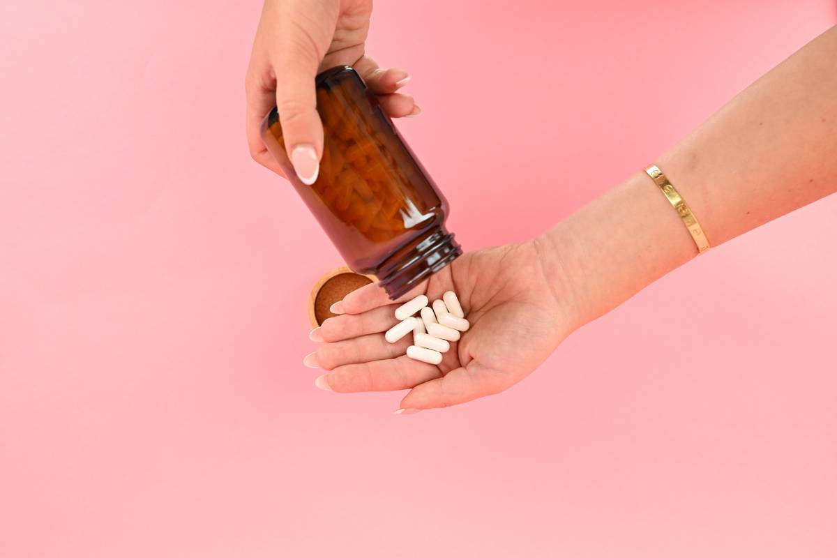 Woman holding a bottle of vitamin supplement for menopause while reviewing ingredient label with sunlight streaming through kitchen window